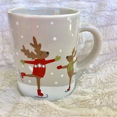 a white coffee mug with reindeers skating in the snow on it's side