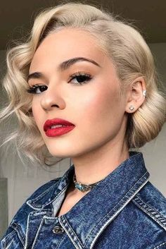 a woman with blonde hair wearing a denim jacket and red lipstick is looking off to the side