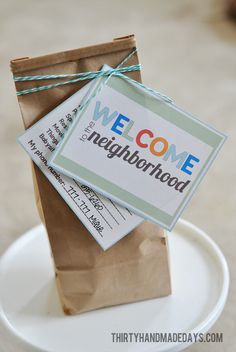 a welcome neighborhood sign is tied to a brown paper bag on a white saucer