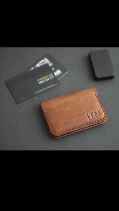 a brown leather wallet sitting next to a cell phone and business card holder on top of a table