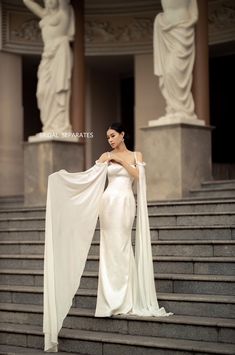 a woman in a white dress standing on some steps with her cape draped over her shoulders