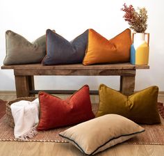 four different colored pillows sitting on top of a wooden bench next to a vase with flowers