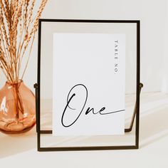 there is a card with the word one in cursive writing next to a vase