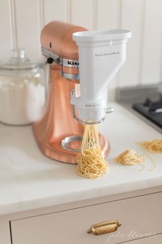 a mixer is being used to make pasta on a counter top with other kitchen appliances in the background