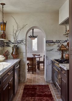 an archway leads into a kitchen with marble counter tops and brown cabinets, along with a red rug on the floor