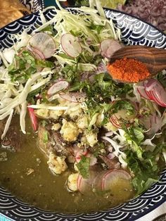 a bowl filled with soup and vegetables on top of a blue plate next to bread