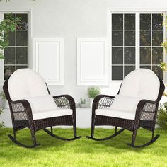 two wicker rocking chairs sitting on top of a green grass covered field next to windows