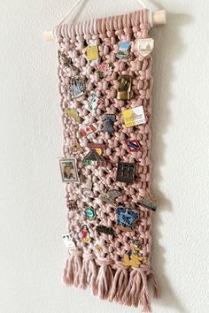 a pink crocheted wall hanging with pins and magnets on it, next to a white wall