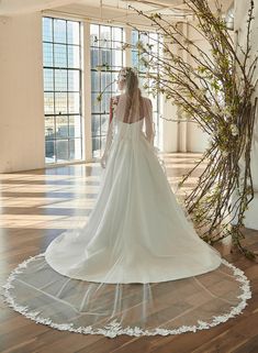 a woman in a white wedding dress standing on a wooden floor next to a tree