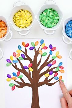 a hand is pointing at a paper tree with candy candies in it and three bowls on the table