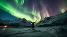 a man standing in the snow with his arms up under an aurora bore above mountains