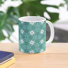 a green and white coffee mug sitting on top of a wooden table next to a book