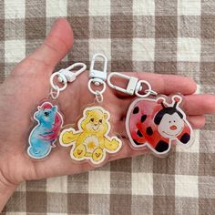 a person's hand holding four key chains with cartoon animals on them, including a ladybug and a bear