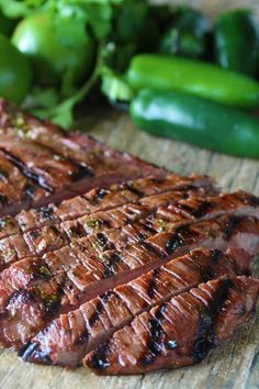 a piece of steak sitting on top of a wooden cutting board next to green peppers