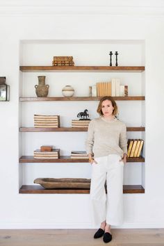 a woman standing in front of a book shelf with books on it and shelves behind her