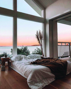 a bed sitting in front of large windows next to a wooden floor covered with white sheets