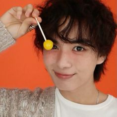 a young man holding a lollipop in front of his face with an orange background