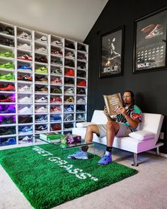 a person sitting on a couch reading a book in front of a wall full of shoes