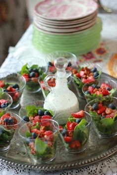 small cups filled with salad on top of a silver tray next to plates and bowls