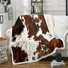 a cow print blanket on a couch in a living room with white walls and wooden floors