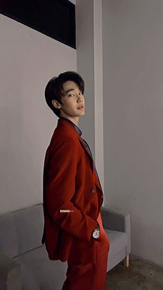 a young man in a red suit standing next to a white wall and looking off into the distance