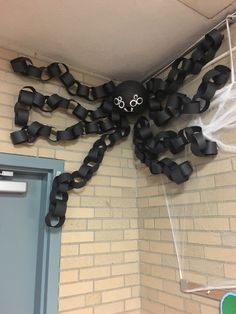 a spider made out of black ribbon hanging from the ceiling in front of a brick wall