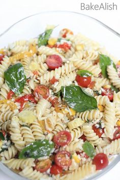 pasta salad with tomatoes, corn and spinach in a glass bowl on a white table