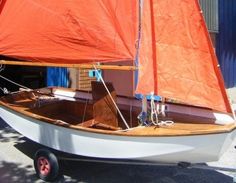 a small sailboat with orange sails is parked in front of a blue building on wheels