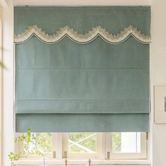 a kitchen window with blue roman shades and white trim on the valance, in front of a sink