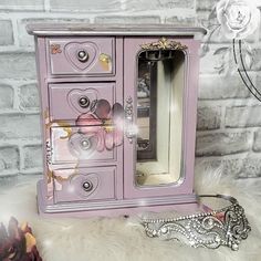 a pink jewelry cabinet sitting on top of a white furnishing next to a mirror