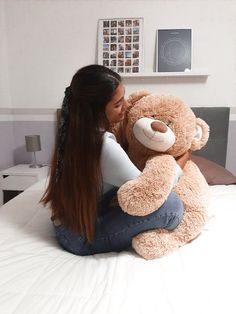 a woman sitting on top of a bed hugging a teddy bear