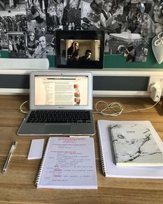 an open laptop computer sitting on top of a wooden desk next to a notebook and pen