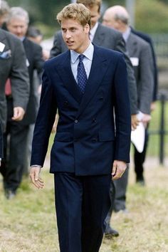 a man in a blue suit and tie walking through the grass with other people behind him