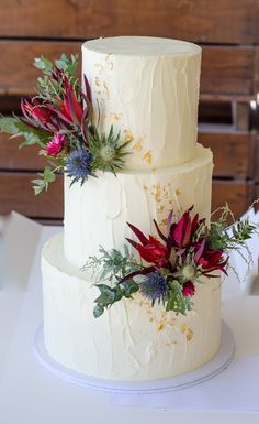 a three tiered white wedding cake with red flowers on the side and greenery