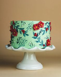 a green cake decorated with red flowers on a white pedestal against a brown background,