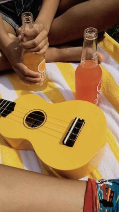 a yellow ukulele sitting on top of a towel next to two bottles of soda