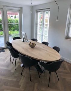 a dining room table with black chairs and a laptop on it in front of two windows