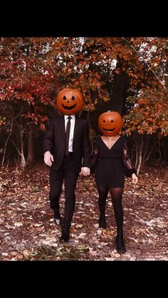 two people in suits and pumpkin heads walking through the woods with leaves on the ground