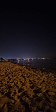 the beach is covered in sand at night with lights shining on the water behind it