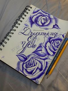 an open notebook with blue roses and the words dreaming are you written on it next to a pencil