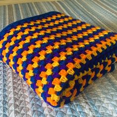 a crocheted blanket sitting on top of a bed with blue and yellow sheets