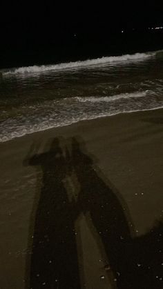 the shadow of a person standing in front of an ocean beach with waves coming in