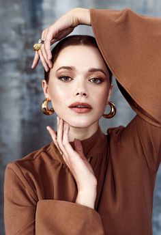 a woman with her hands on her head and wearing large gold hoop earrings, posing for the camera