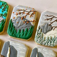 four decorated cookies sitting on top of a white table next to trees and snow covered mountains