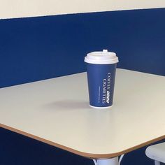 a cup of coffee sitting on top of a table next to a white chair and blue wall