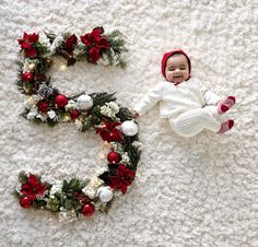 a baby laying on top of a white rug next to wreaths and christmas decorations