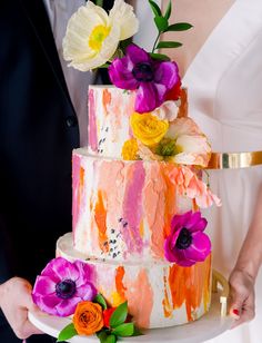 a bride and groom holding a multi - tiered wedding cake with flowers on top