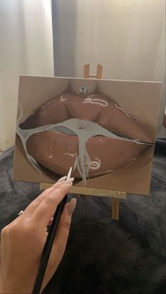 a person is drawing on a piece of cardboard with white paint and a pencil in their hand