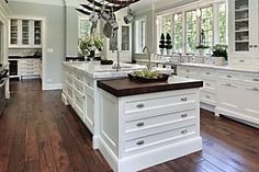 a large kitchen with wooden floors and white cabinets on the walls, along with an island in the middle