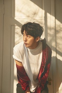 a young man sitting on top of a wooden bench next to a white door wearing a red and black jacket